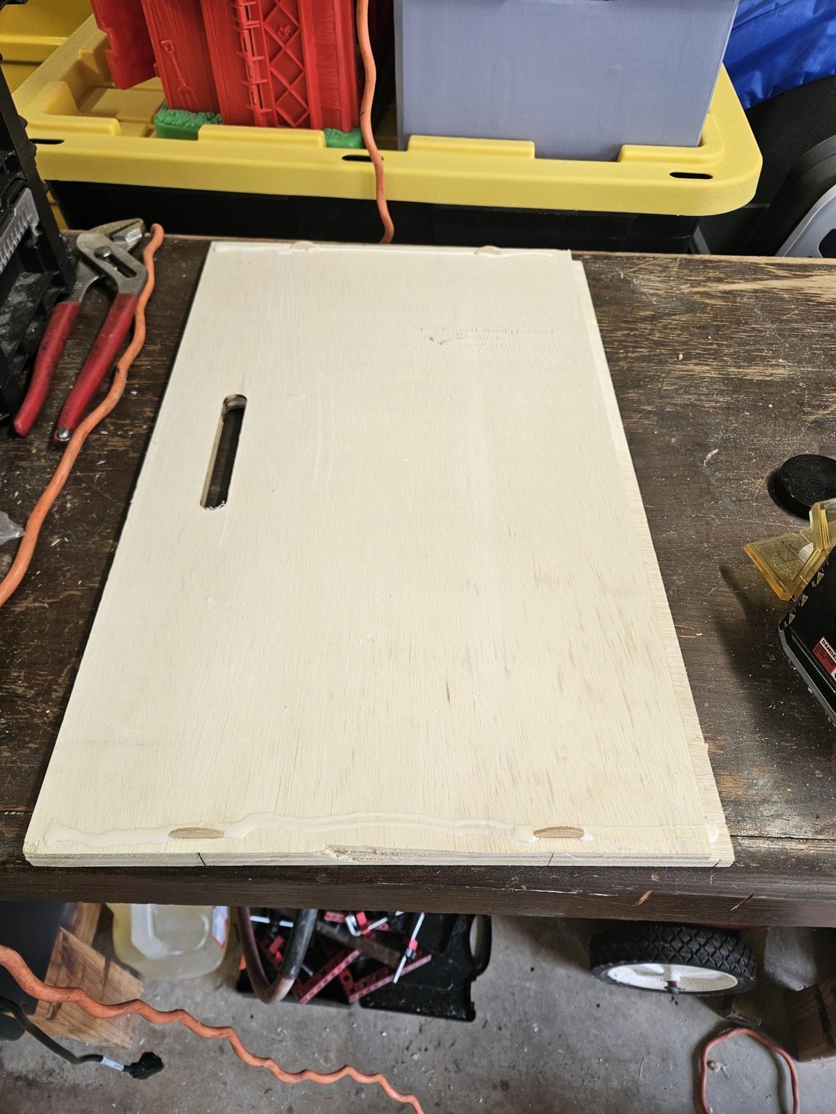 A drawer wall on the bench with glue along one edge, two biscuits in their slots, and a cord slot cut through the panel